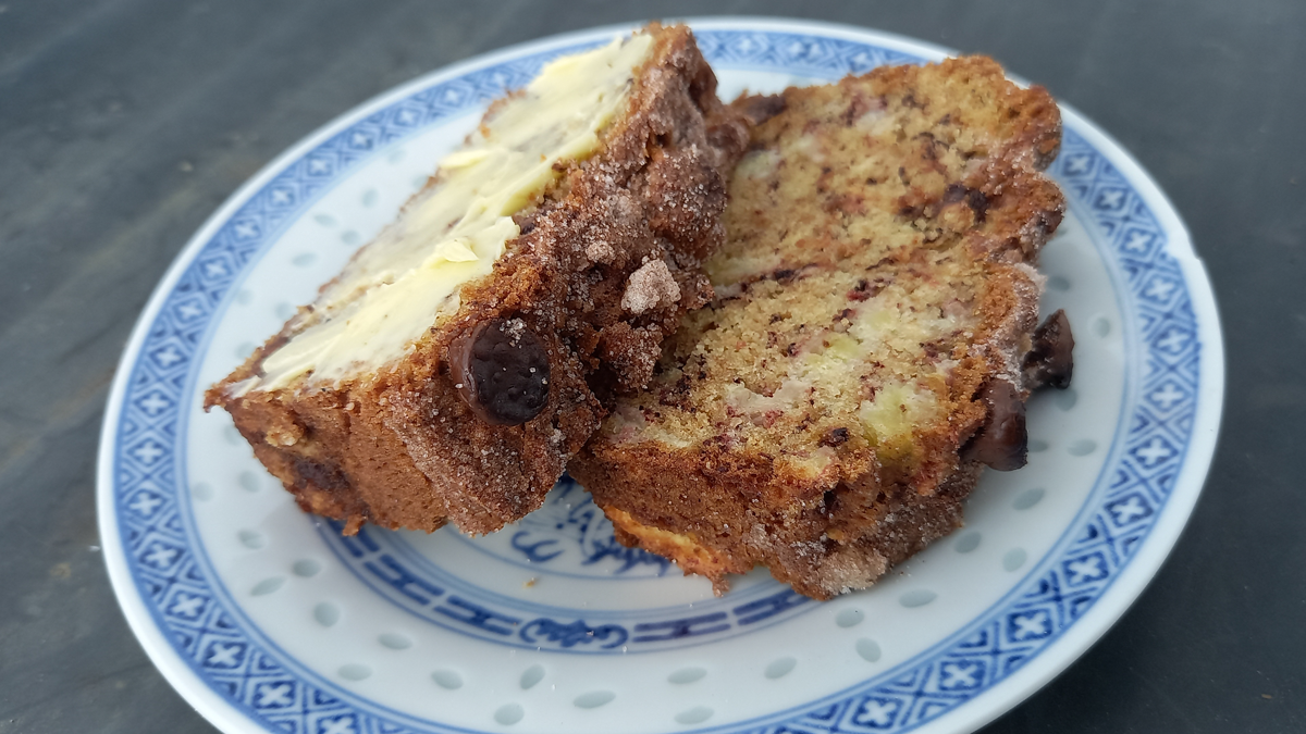 Two slices of banana bread - one smothered in butter - on a plate.
