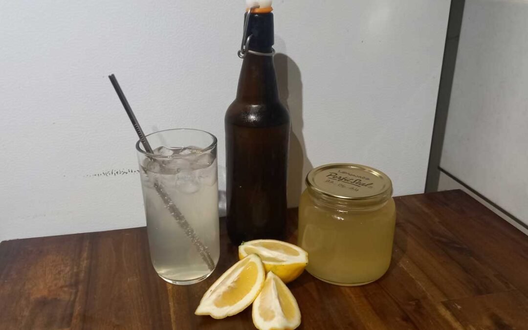 A glass of lemonade, a bottle and can of syrup, and a lemon.