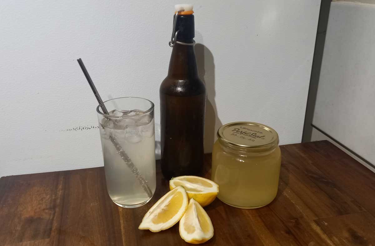 A glass of lemonade, a bottle and can of syrup, and a lemon.