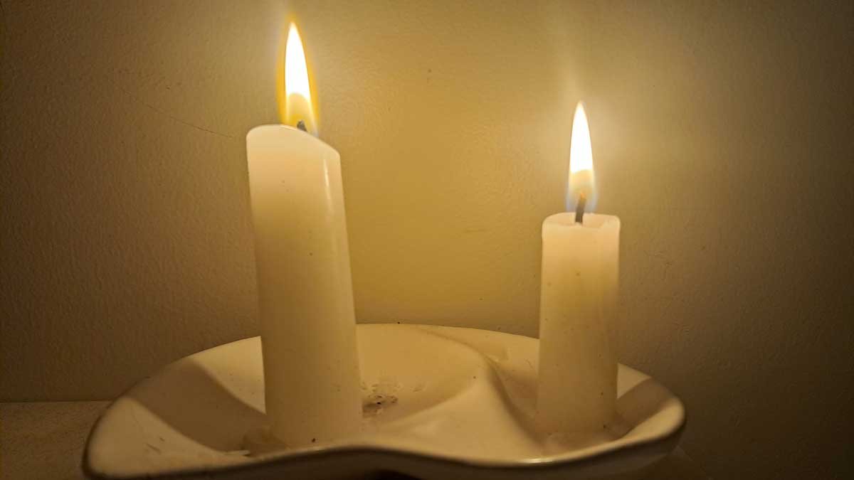 Two short candles burning in a dish.