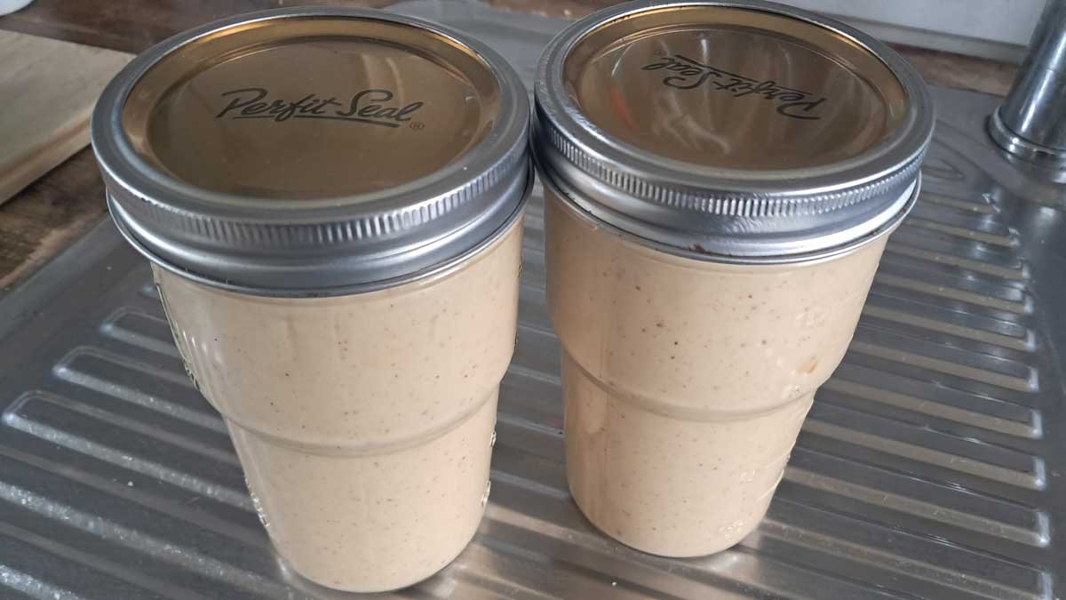 Two jars of peanut butter on a stainless steel bench.