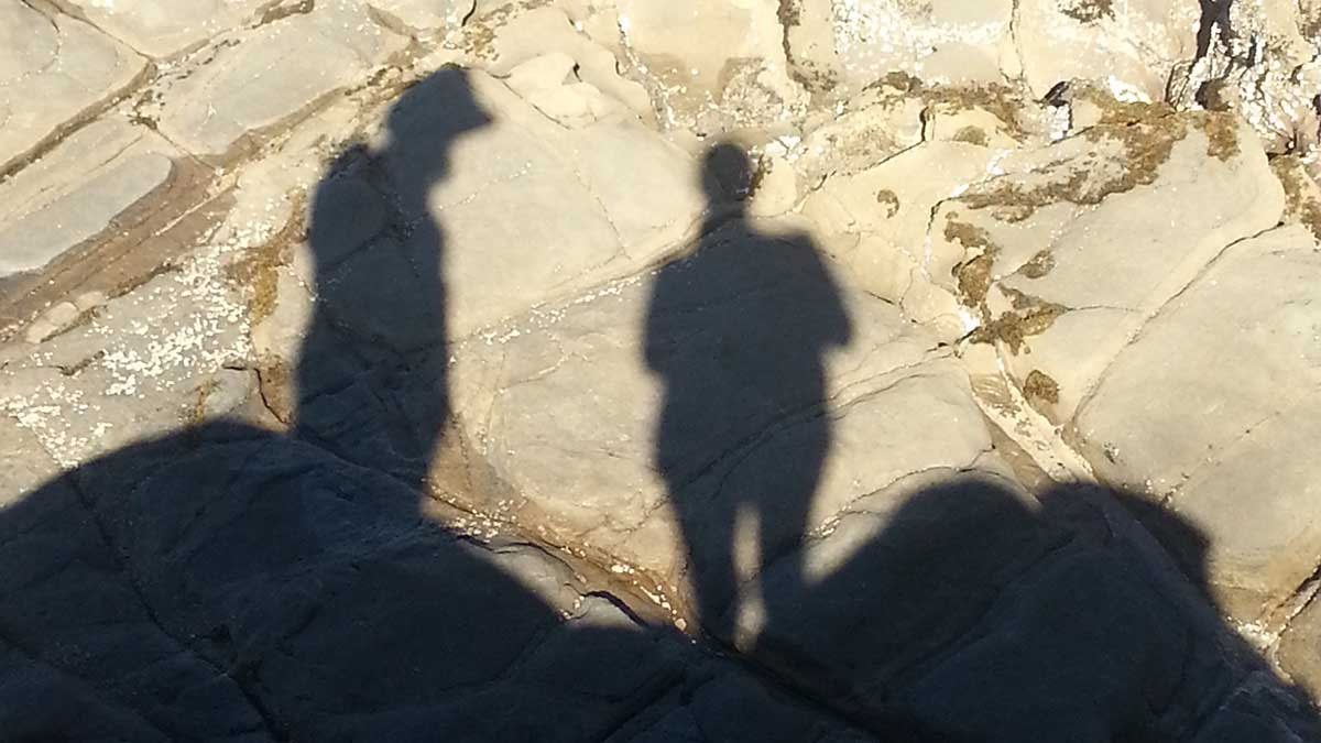 Shadow of a man in a hat and a woman against rocks.