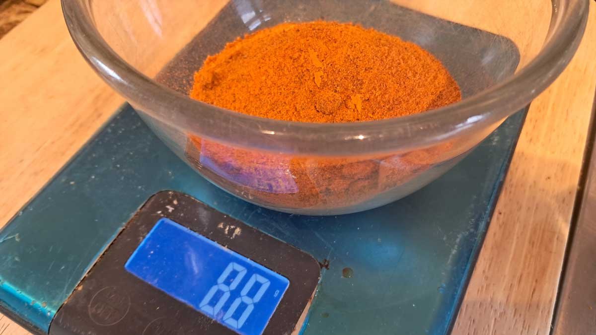 A glass bowl of smoked paprika powder on a scale that reads 88 grams.