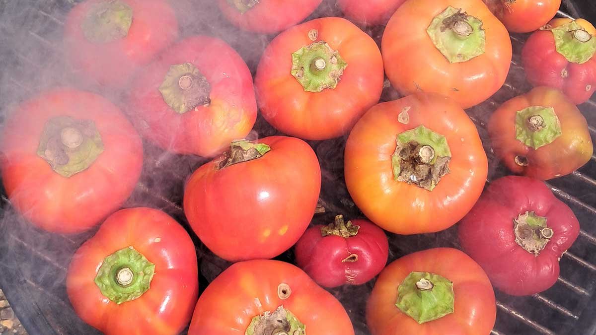 Paprika fruit on a charcoal barbeque with smoke drifting over them.