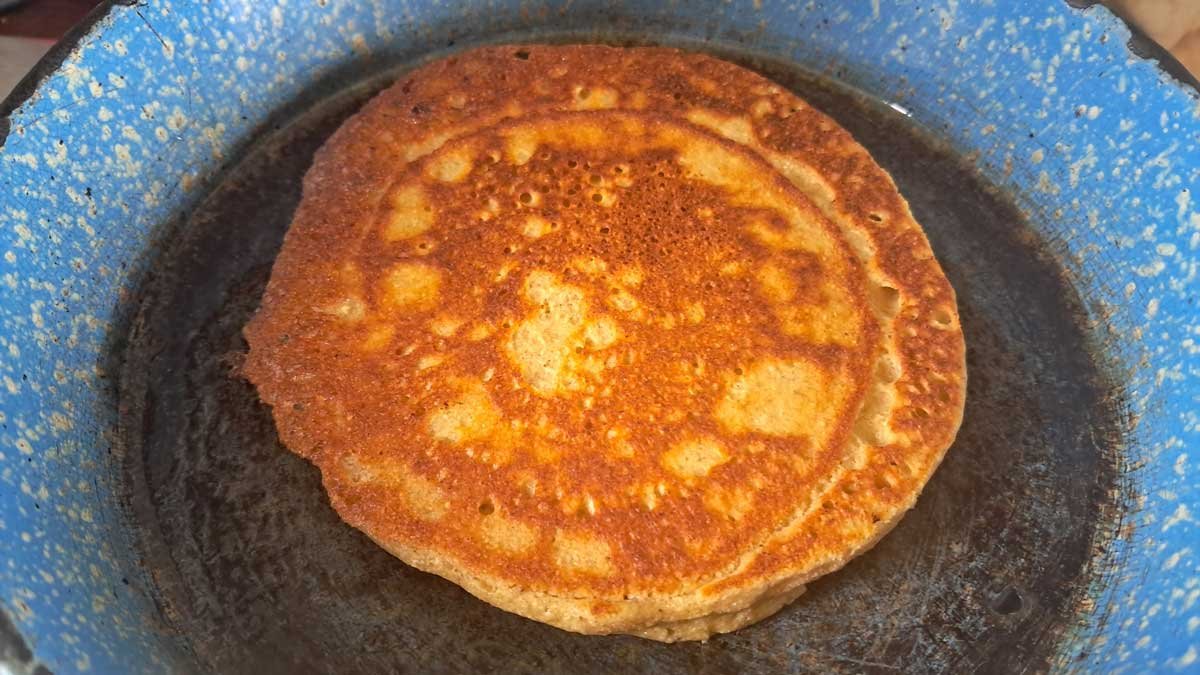 Golden green banana flour pancake on a blue enamel frying pan.