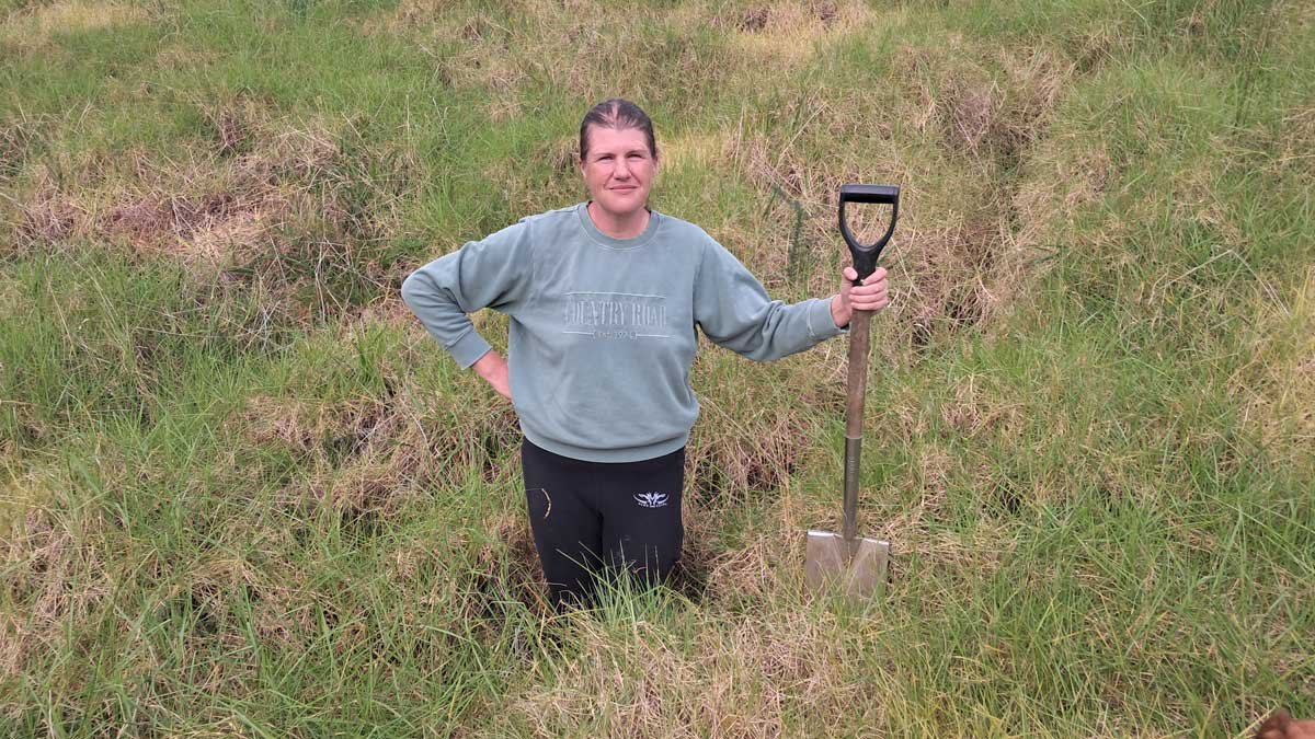 Kat standing thigh-deep inside the drainage path, with a spade resting on the soil level.